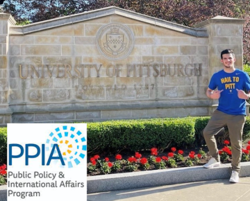 Student poses on campus with main University sign 