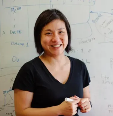 "Professor Sera Linardi holds a marker in front of a whiteboard full of graphs and equations"
